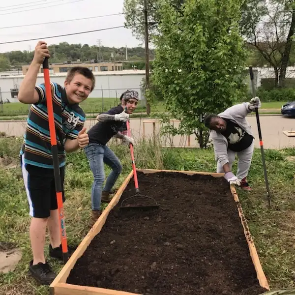 Two adults and one child happily spreading dirt in a raised garden bed at the South Cumminsville Community Garden.