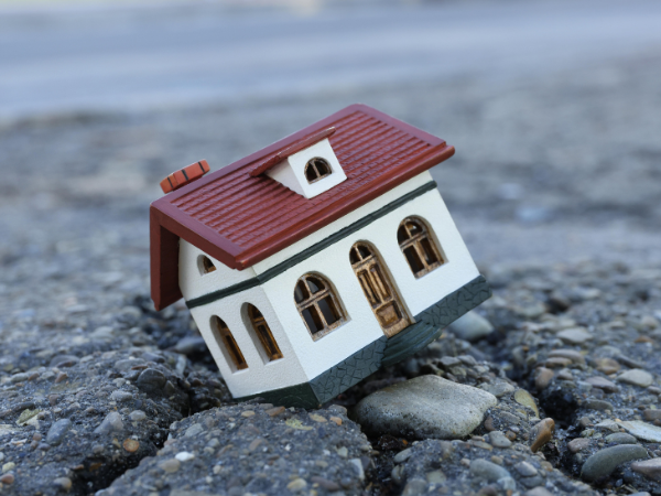 A replica home sits crooked on some rainy stones representing the importance of preparing for disasters.